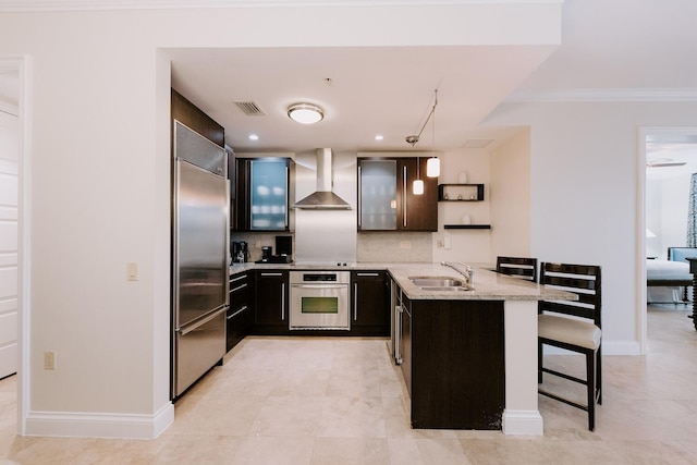 kitchen with visible vents, appliances with stainless steel finishes, a breakfast bar, wall chimney range hood, and a sink