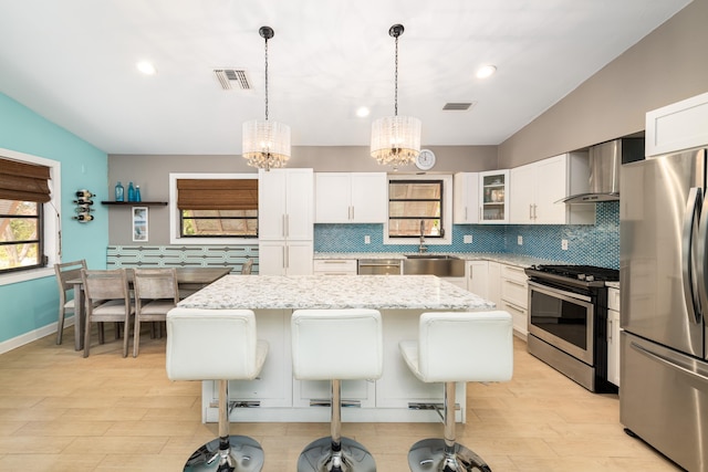 kitchen with wall chimney exhaust hood, appliances with stainless steel finishes, a kitchen island, and visible vents