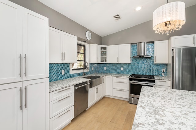 kitchen with appliances with stainless steel finishes, vaulted ceiling, a sink, light stone countertops, and wall chimney exhaust hood