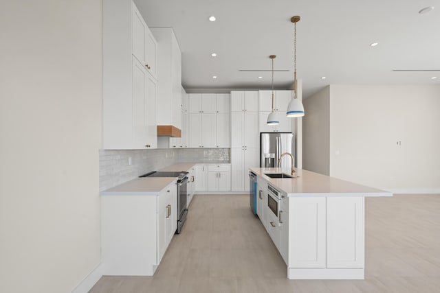 kitchen with a center island with sink, stainless steel appliances, pendant lighting, sink, and white cabinetry