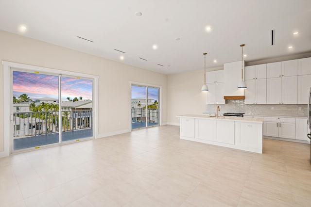 kitchen with a center island with sink, sink, pendant lighting, white cabinets, and tasteful backsplash