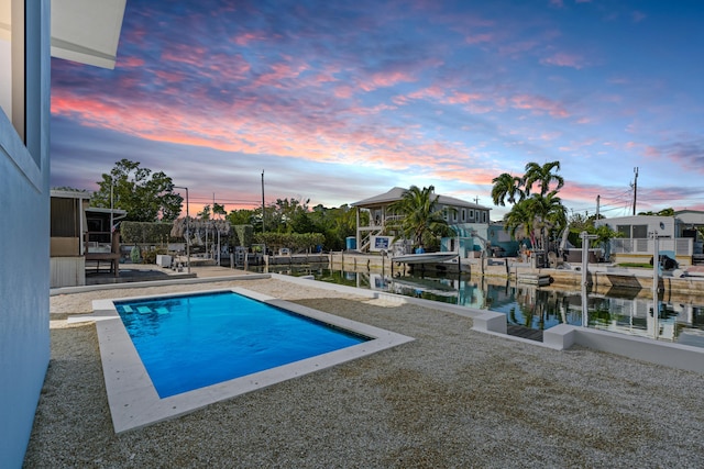 pool at dusk featuring a patio and a water view