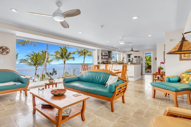 living room featuring stone tile floors, recessed lighting, a water view, a ceiling fan, and baseboards