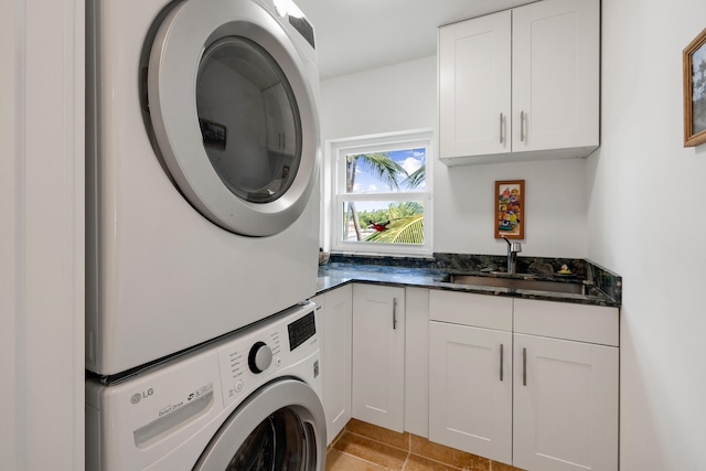 clothes washing area featuring light tile patterned floors, stacked washing maching and dryer, a sink, and cabinet space