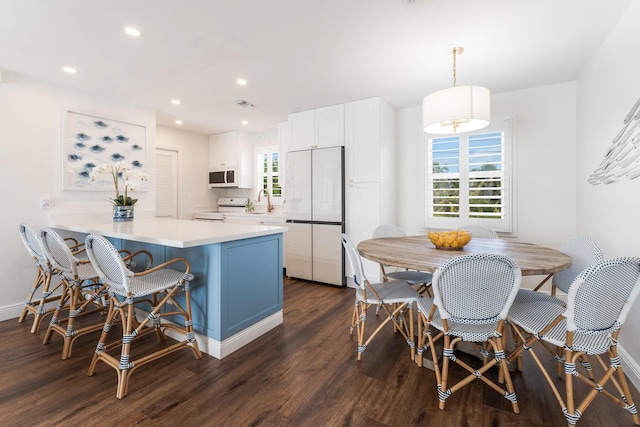 kitchen with dark hardwood / wood-style floors, white cabinetry, hanging light fixtures, kitchen peninsula, and white appliances