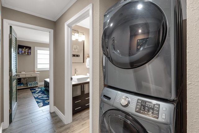 laundry room featuring crown molding, stacked washer and clothes dryer, light hardwood / wood-style floors, and sink