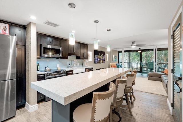 kitchen featuring dark brown cabinetry, tasteful backsplash, hanging light fixtures, appliances with stainless steel finishes, and a kitchen island