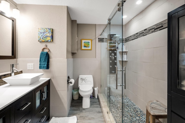 bathroom with tile walls, hardwood / wood-style flooring, vanity, walk in shower, and toilet