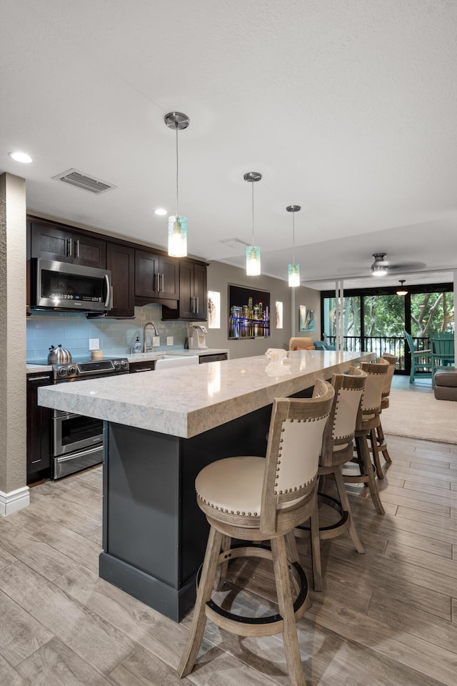 kitchen with decorative light fixtures, a breakfast bar area, stainless steel appliances, dark brown cabinets, and a spacious island