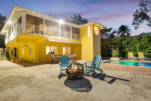 back house at dusk with a fenced in pool, a balcony, a patio area, and a fire pit