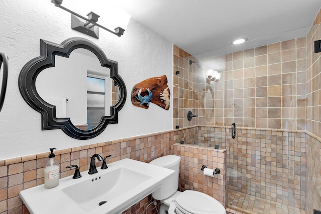 bathroom featuring a sink, a shower stall, wainscoting, tile walls, and toilet