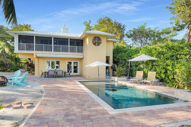 rear view of property featuring french doors, a sunroom, a patio, and an outdoor fire pit