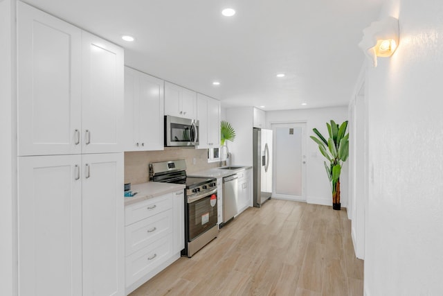 kitchen with stainless steel appliances, light countertops, white cabinetry, a sink, and light wood-type flooring