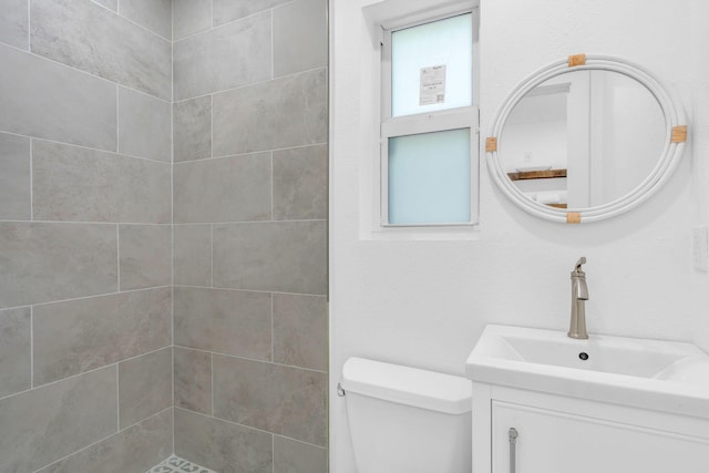 bathroom with a tile shower, vanity, and toilet