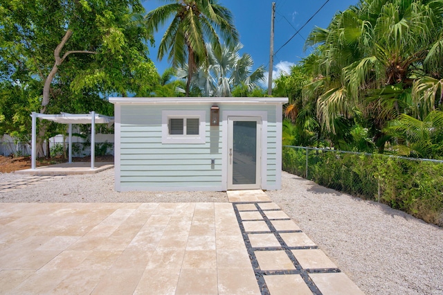 view of outbuilding featuring fence, a pergola, and an outbuilding