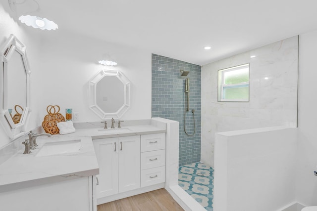 bathroom with a walk in shower, double vanity, wood finished floors, and a sink