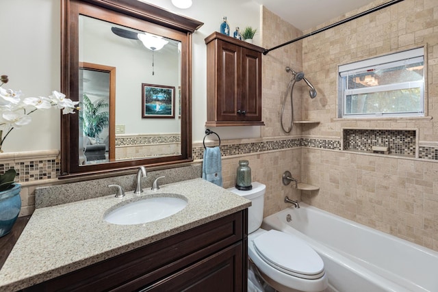 bathroom featuring toilet, a wainscoted wall, vanity, tile walls, and shower / washtub combination