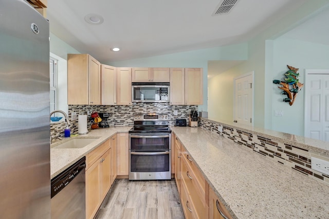 kitchen featuring lofted ceiling, sink, appliances with stainless steel finishes, light stone countertops, and light brown cabinets