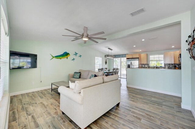 living room with vaulted ceiling, ceiling fan, and light wood-type flooring