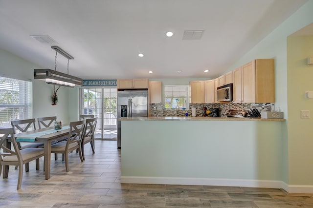 kitchen featuring light brown cabinetry, backsplash, pendant lighting, and stainless steel appliances