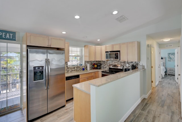 kitchen featuring stainless steel appliances, light brown cabinetry, kitchen peninsula, and decorative backsplash