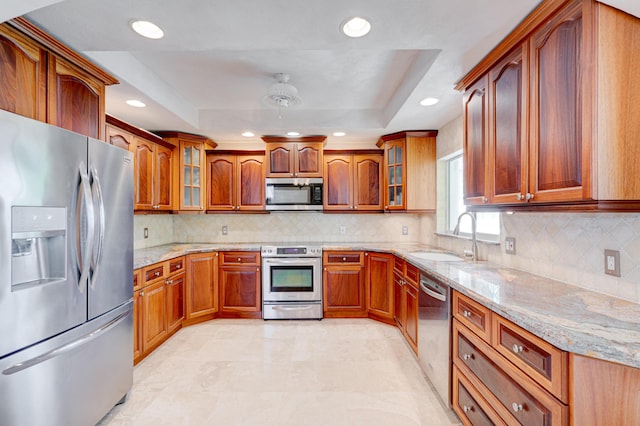 kitchen featuring stainless steel appliances, a raised ceiling, light stone countertops, and sink