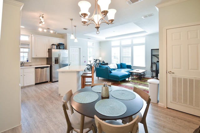 dining space featuring crown molding, a tray ceiling, and light wood-type flooring