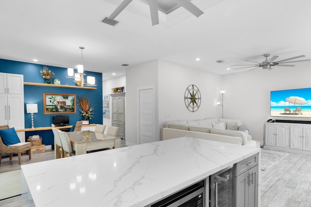 kitchen with light hardwood / wood-style flooring, white cabinetry, wine cooler, light stone countertops, and decorative light fixtures