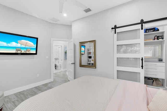 bedroom featuring connected bathroom, a barn door, ceiling fan, and light wood-type flooring