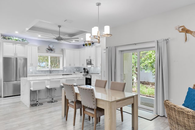 dining space with ceiling fan with notable chandelier, light hardwood / wood-style floors, and a raised ceiling