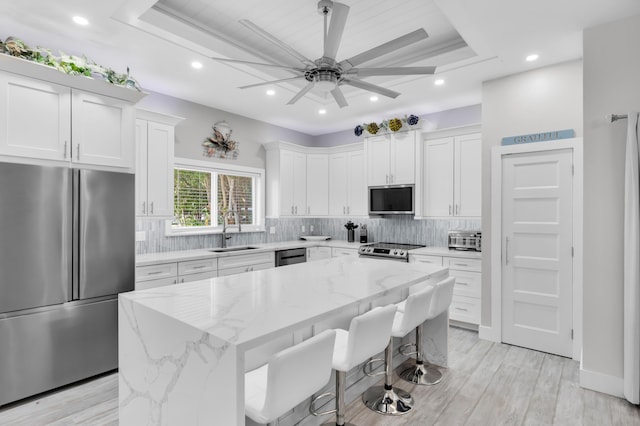 kitchen featuring white cabinetry, stainless steel appliances, a center island, and light stone countertops