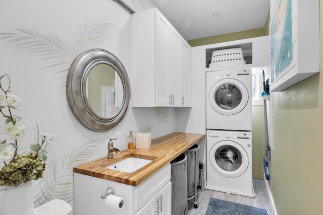 laundry area with sink, stacked washer and clothes dryer, and light wood-type flooring