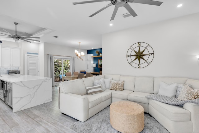 living room with ceiling fan with notable chandelier and light hardwood / wood-style flooring