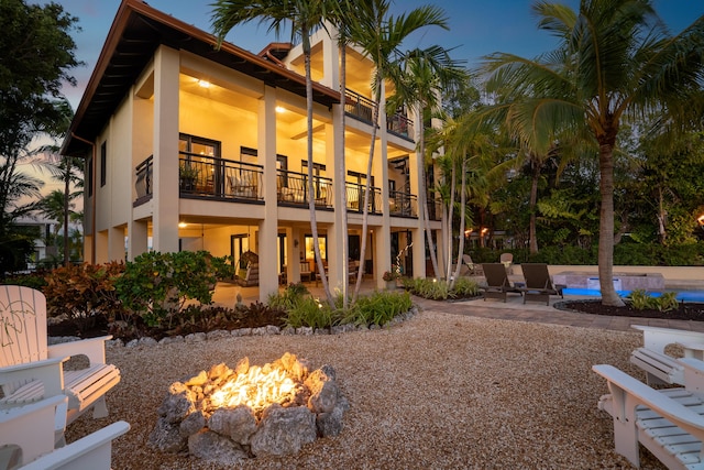 back house at dusk featuring a fire pit, a patio area, and a balcony