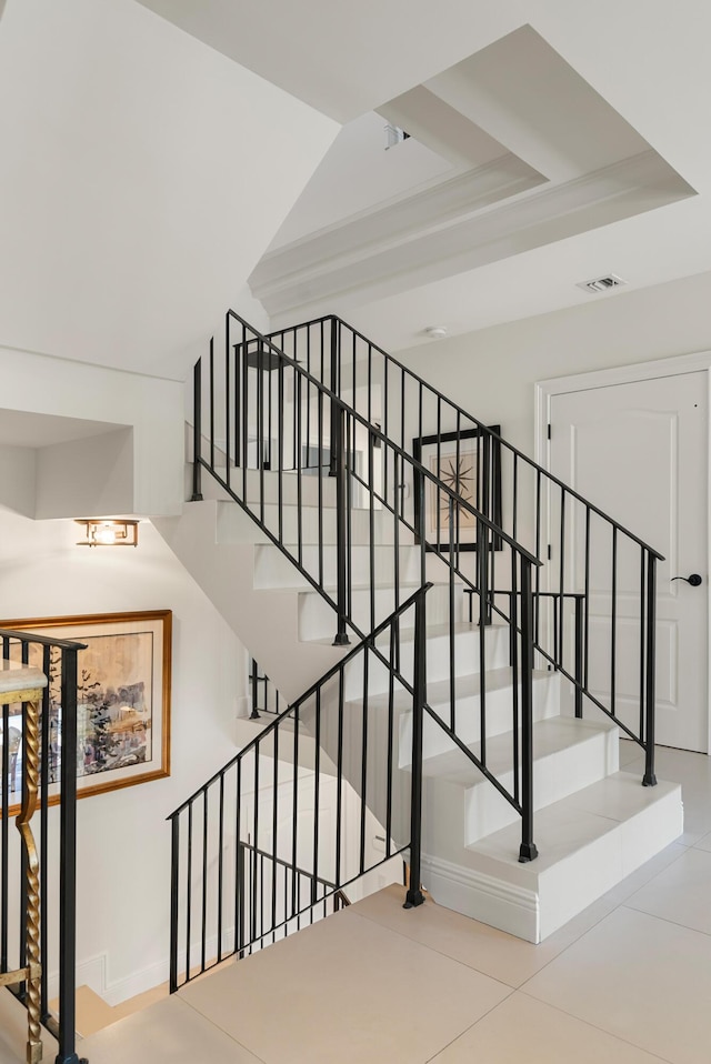 staircase with a raised ceiling and tile patterned floors