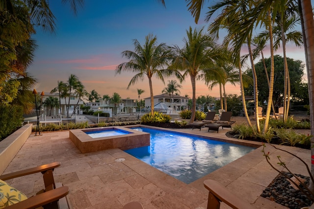 pool at dusk featuring an in ground hot tub and a patio area