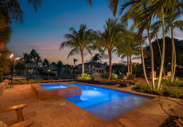 pool at dusk featuring a patio area and an in ground hot tub