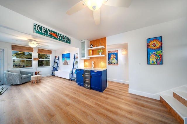 kitchen with light stone counters, ceiling fan, blue cabinets, and light wood-type flooring