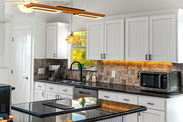 kitchen featuring appliances with stainless steel finishes, sink, white cabinets, backsplash, and dark stone counters