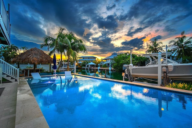 pool at dusk featuring a boat dock and a water view