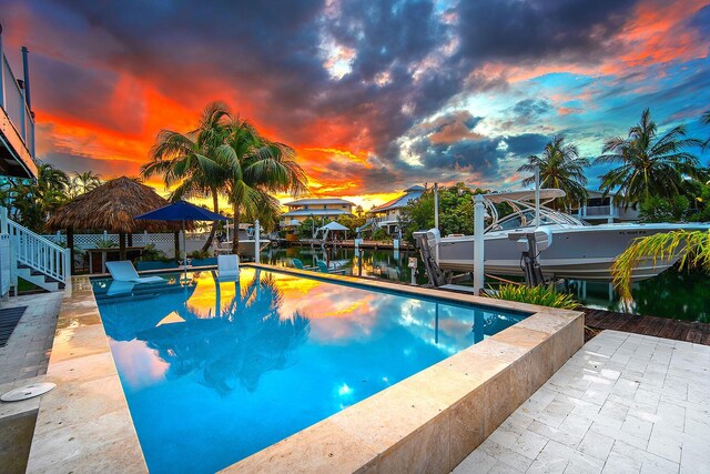 pool at dusk featuring a boat dock and a water view