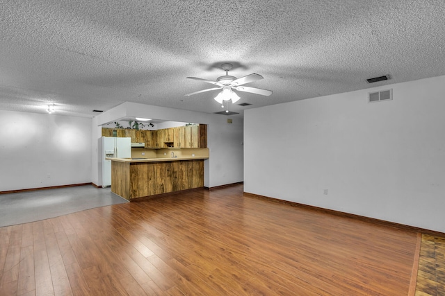 unfurnished living room featuring ceiling fan, a textured ceiling, wood finished floors, visible vents, and baseboards