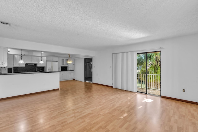 unfurnished living room featuring visible vents, light wood-style floors, a sink, a textured ceiling, and baseboards