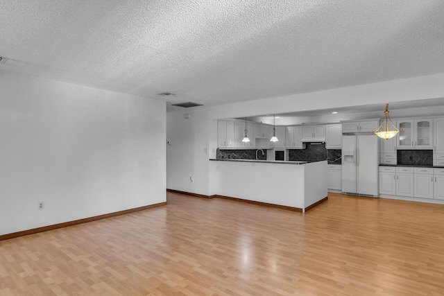 unfurnished living room featuring light wood-type flooring, a textured ceiling, baseboards, and a sink