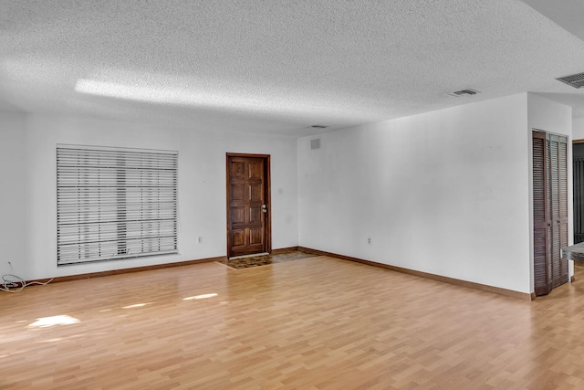 unfurnished room featuring light wood-style floors, visible vents, a textured ceiling, and baseboards