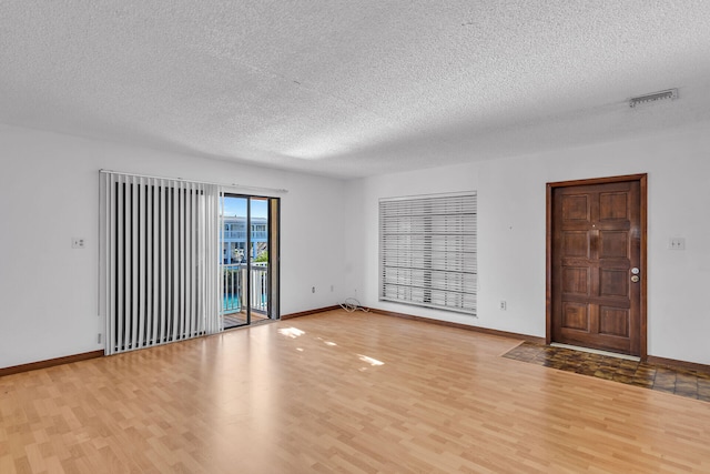 empty room featuring light wood-type flooring, visible vents, baseboards, and a textured ceiling