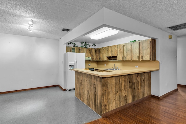 kitchen with a peninsula, white refrigerator with ice dispenser, a sink, light countertops, and brown cabinets