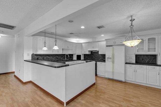 kitchen featuring hanging light fixtures, white refrigerator with ice dispenser, dark countertops, and white cabinets