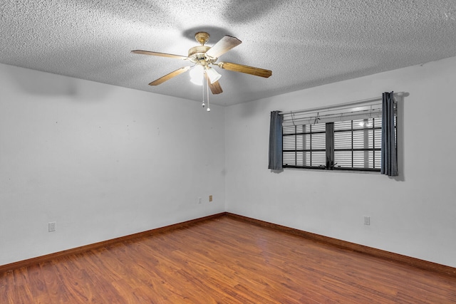 empty room with a textured ceiling, wood finished floors, a ceiling fan, and baseboards