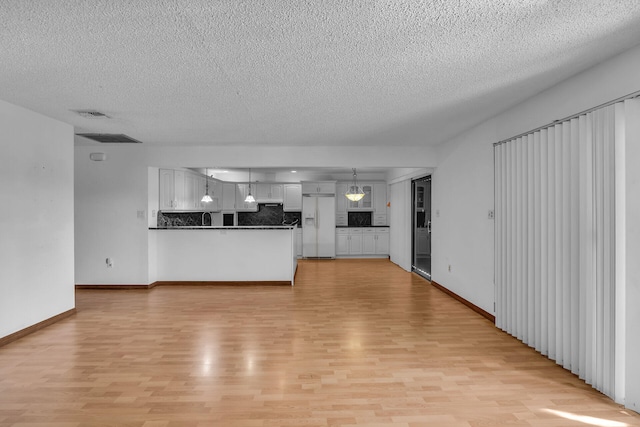 unfurnished living room featuring baseboards, visible vents, light wood-style flooring, and a textured ceiling